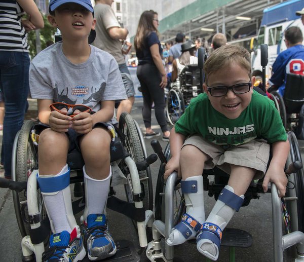 an image of 2 kids in a wheelchair smiling in the Disability Pride Parade