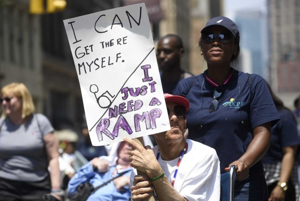 A participant holds a sign saying "I can get there myself, I just need a ramp."