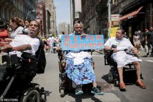 Three people in wheelchairs marching in the NYC Disability Pride Parade. One holding a sign saying 'Better Together'