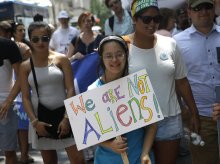 A girl holds a sign that says 'We Are Not Aliens' and prepares to march in the NYC Disability Pride Parade. 