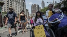 People participate in the first annual Disability Pride Parade. Two wheelchair users in front and dozens of people marching behind.