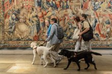 4 people walking in front of a mural with two service animals 