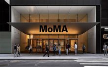 An photo of the front entrance of the Museum of Modern Art with people walking in front of it.