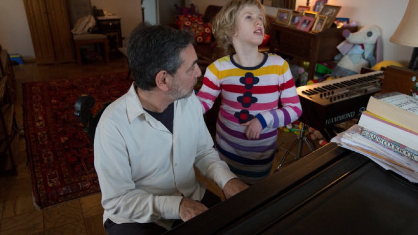 An adult and child in front of a grand piano practicing.