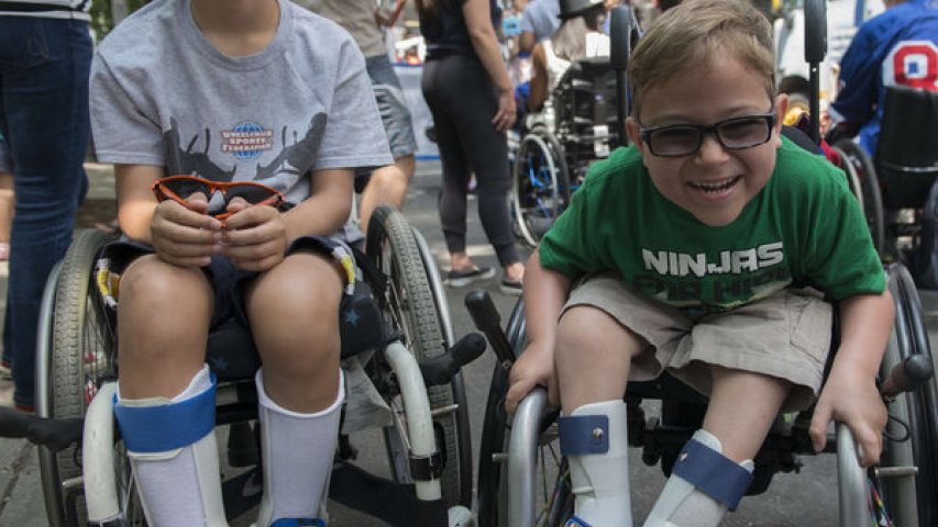 an image of 2 kids in a wheelchair smiling in the Disability Pride Parade