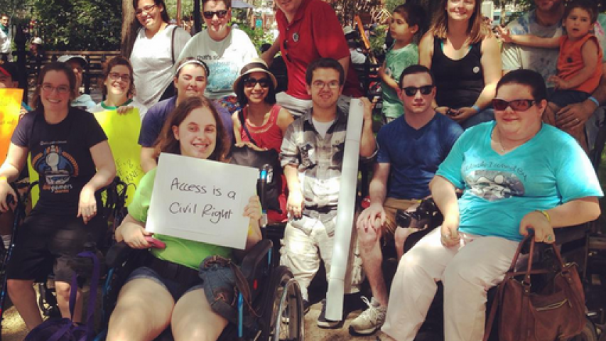 A group of people taking a picture together while one is holding a sign saying "access is a civil right"