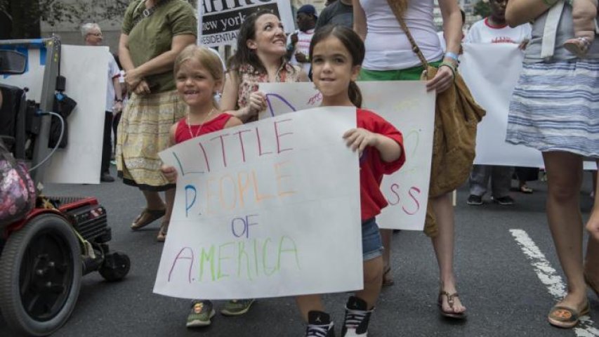 Two people holding a sign "Little People of America"