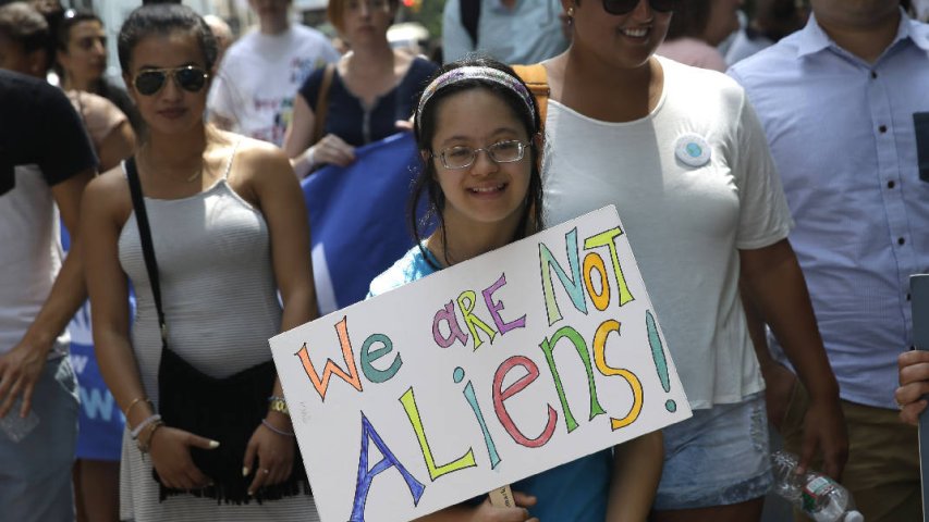 A girl holds a sign that says 'We Are Not Aliens' and prepares to march in the NYC Disability Pride Parade. 
