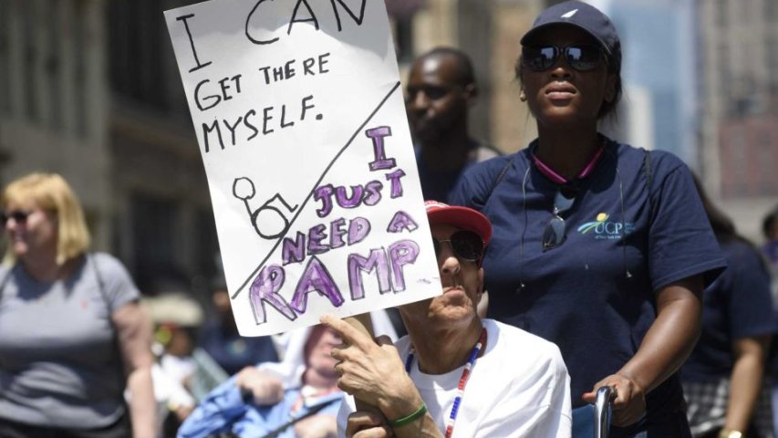 A participant holds a sign saying "I can get there myself, I just need a ramp."